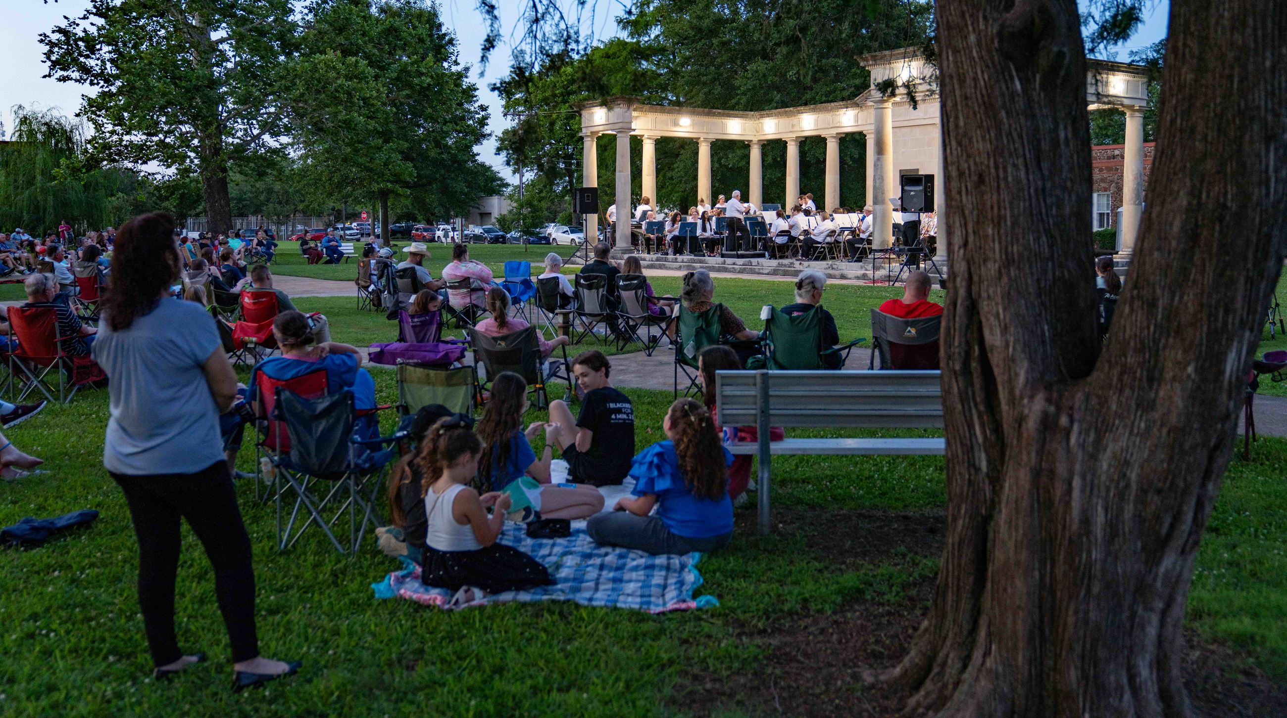 Group of people in law chairs and sitting on blankets watch Paris Municipal Band in Bywaters Park